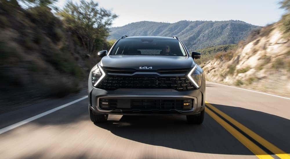 A gray 2024 Kia Sportage shown driving a paved mountain road head-on.
