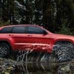 red jeep grand cherokee driving through large puddle