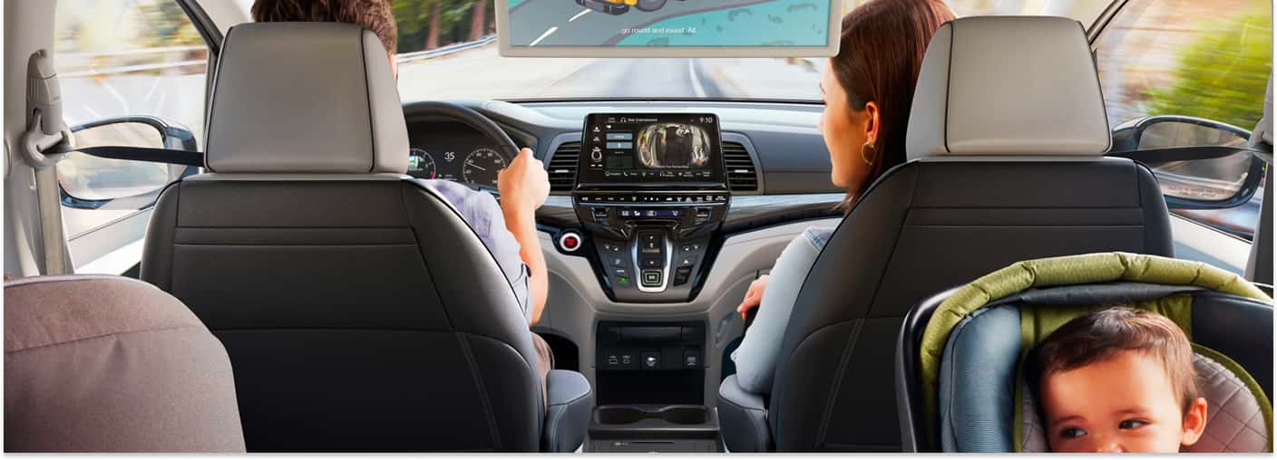 Interior cabin view of a 2026 Honda Odyssey showing gray leather seats, center touchscreen, and overhead rear screen.