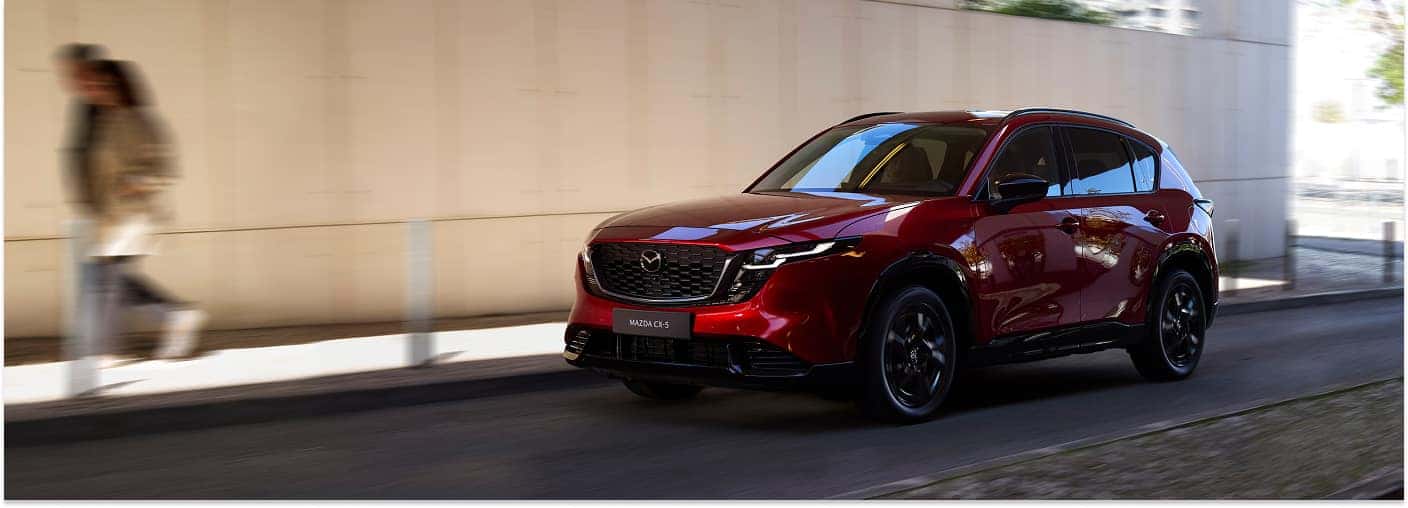 Red 2026 Mazda CX-5 crossover driving along a street in front three-quarter view.