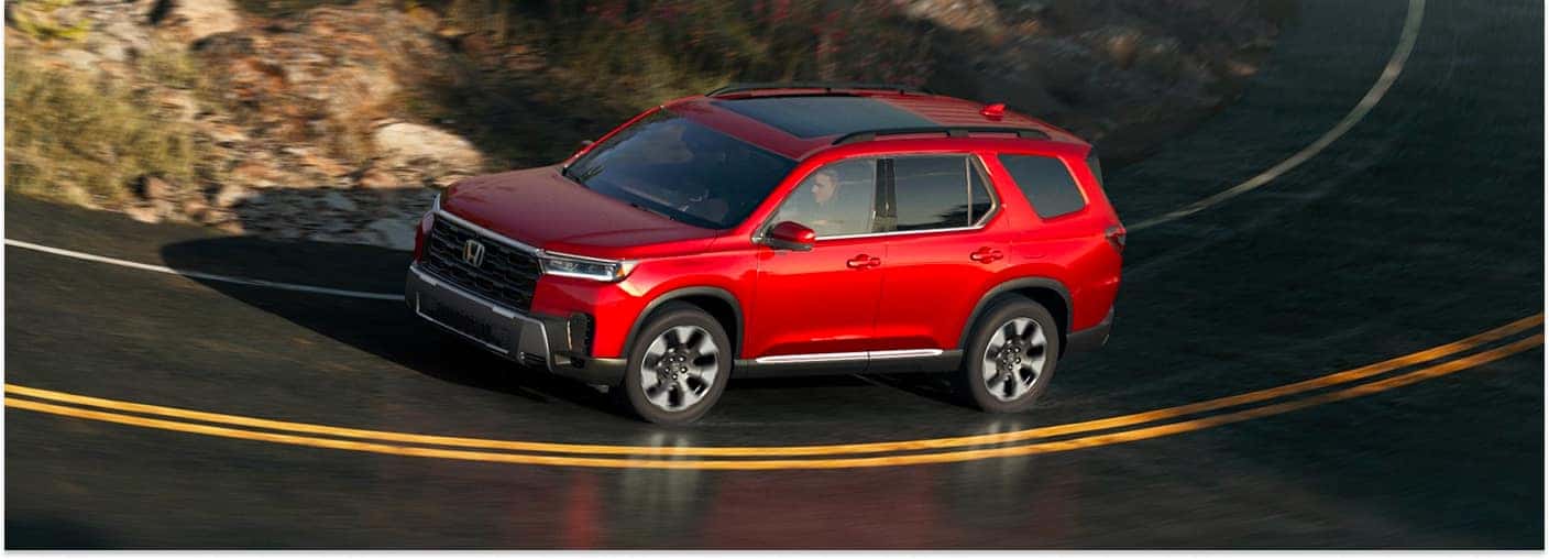 High-angle front three-quarter view of a red 2026 Honda Pilot driving on a winding road.