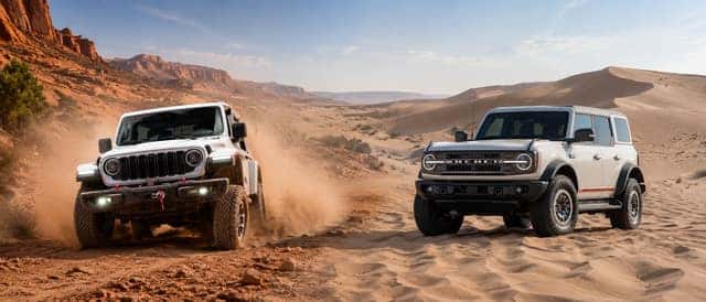 2026 Jeep Wrangler vs. Ford Bronco off-road SUV comparison in rugged desert terrain.